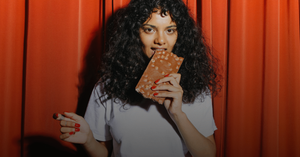 A girl eating chocolate bar with shocking reaction.