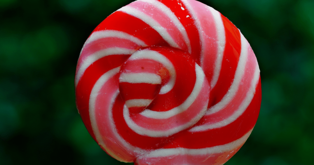 A red and white swirled lollipop resting on a plain background, showcasing its vibrant colors and round shape.