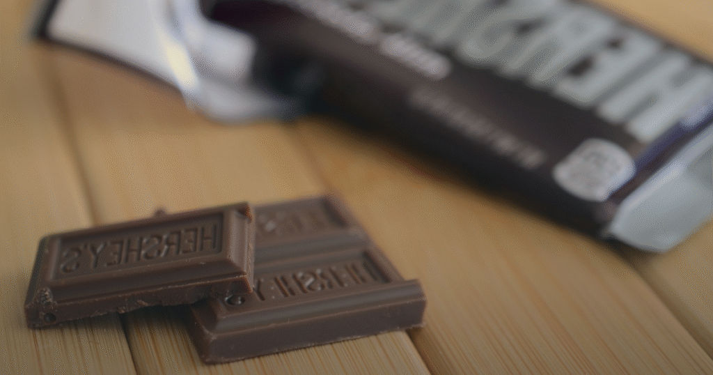A chocolate bar partially unwrapped, resting on a table next to its colorful wrapper.