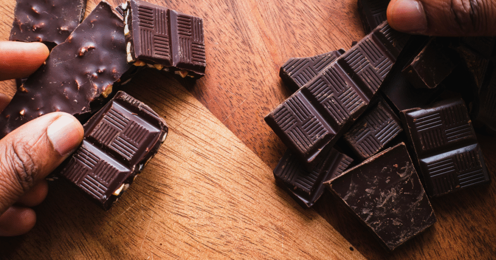 Hands holding various chocolate bars on a rustic wooden table, showcasing a delightful assortment of treats.