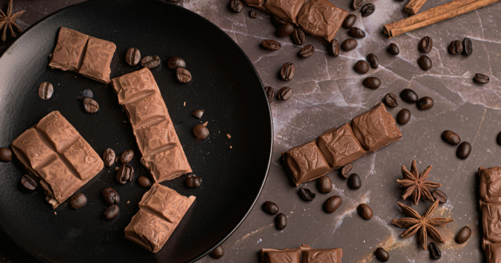 A black plate holds an assortment of chocolate bars and scattered coffee beans, creating a rich, indulgent display.